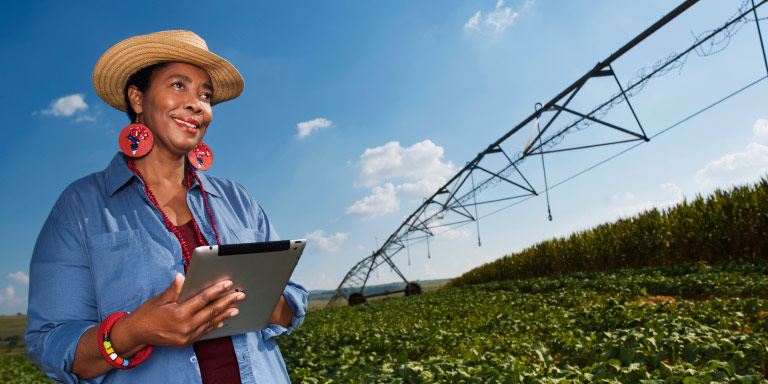 A woman farmer stands amidst her crops, holding a tablet device.